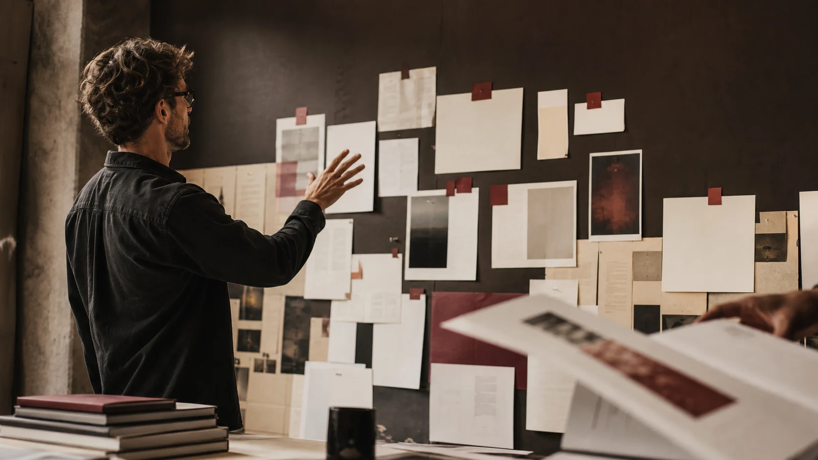 A man pinning printed pages and cards to a wall of reference material